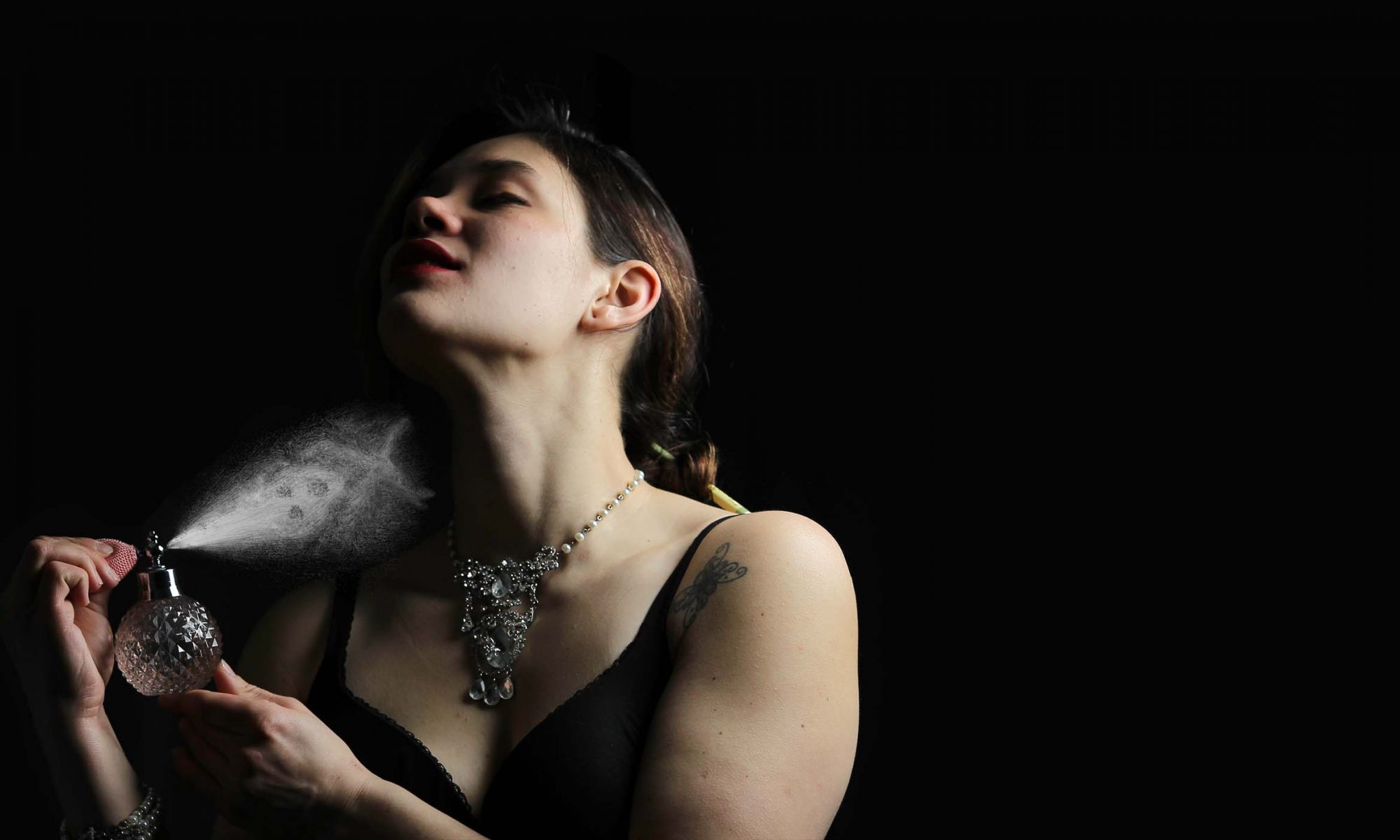 Woman spraying perfume cloud at herself in the shape of a skull and cross bones.